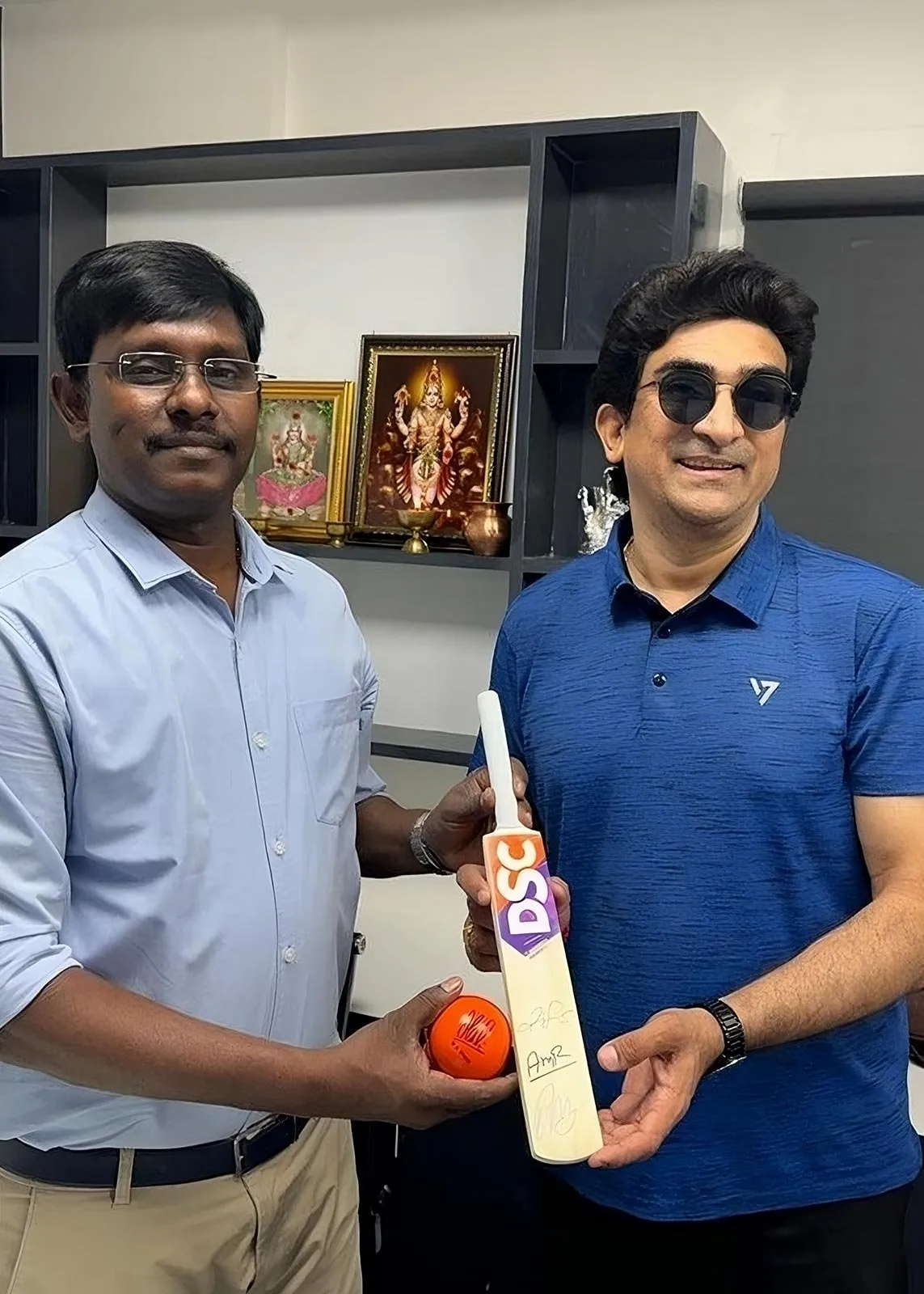 Two men holding a signed cricket bat and a ball between them in an office at the clinic.